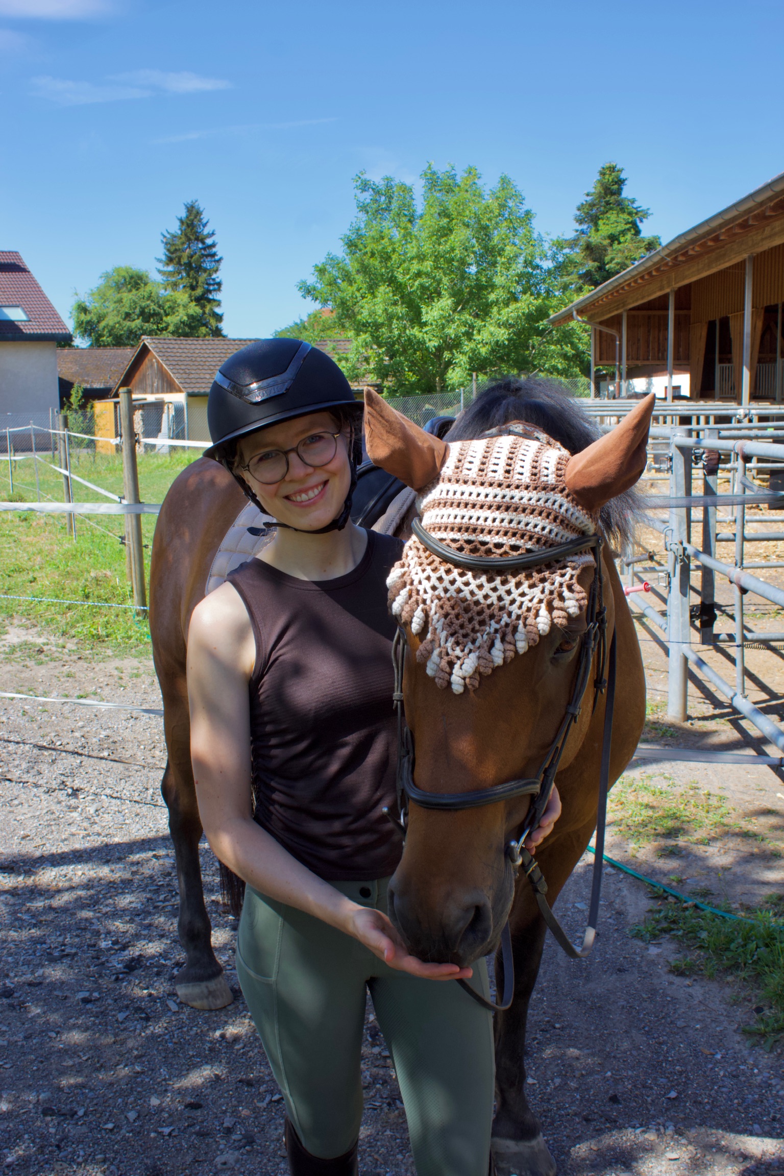 Aline lächelt neben ihrem braunen Pferd und hält eine Hand unter sein Maul
